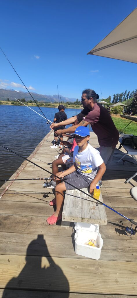 Fishing instructor helping children cast their lines from a wooden dock during a sunny day at Mikhail’s birthday party at Le Bonheur.