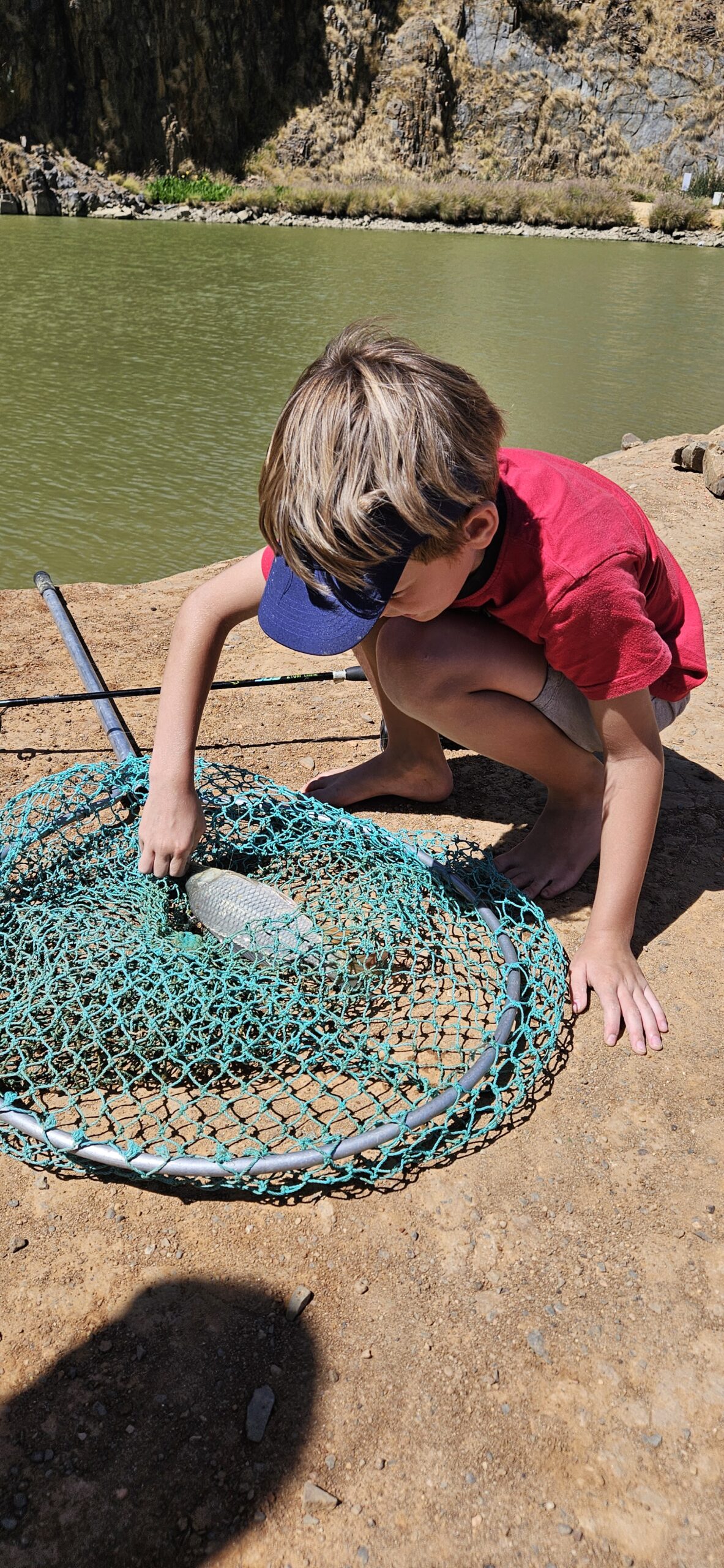 Young boy named Geordi crouched by a net, carefully taking out a fish he caught during a Catch Club session at Hillcrest Quarry on 7 December 2025.